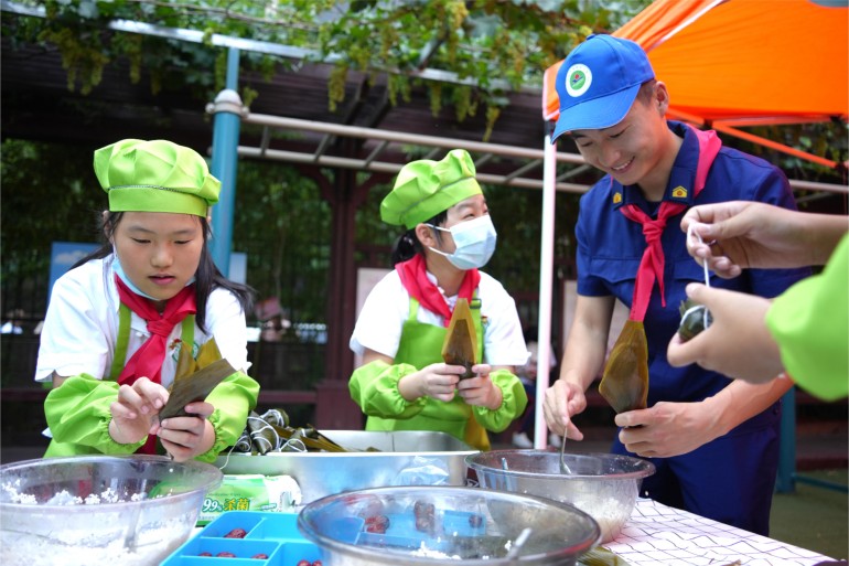 6月21日，濟南館驛街小學舉辦“皂莢樹下話端午”公益愛心主題活動。校內幾棵皂莢樹下，市中消防大隊的“藍朋友”們和少先隊員們一起體驗著包粽子的時光。張源源 陳志偉攝
