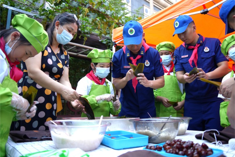 6月21日，濟南館驛街小學舉辦“皂莢樹下話端午”公益愛心主題活動。校內幾棵皂莢樹下，市中消防大隊的“藍朋友”們和少先隊員們一起體驗著包粽子的時光。張源源 陳志偉攝