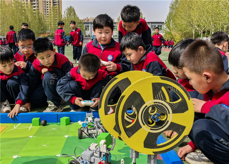 2025年4月16日，山東省樂陵市市中街道阜平小學科技勞動周現場，小學生在通過無線指令遙控“機器人”做游戲。