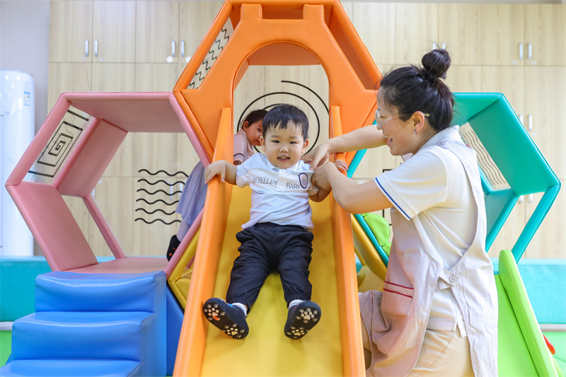2025年5月14日，在山東省青島市李滄區職工子女愛心托育中心，小朋友在老師的陪伴下玩滑梯。張鷹 攝